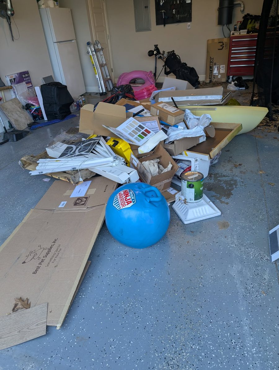 A garage floor covered with flattened boxes, window blinds, a paint can and other clutter piled up for pickup