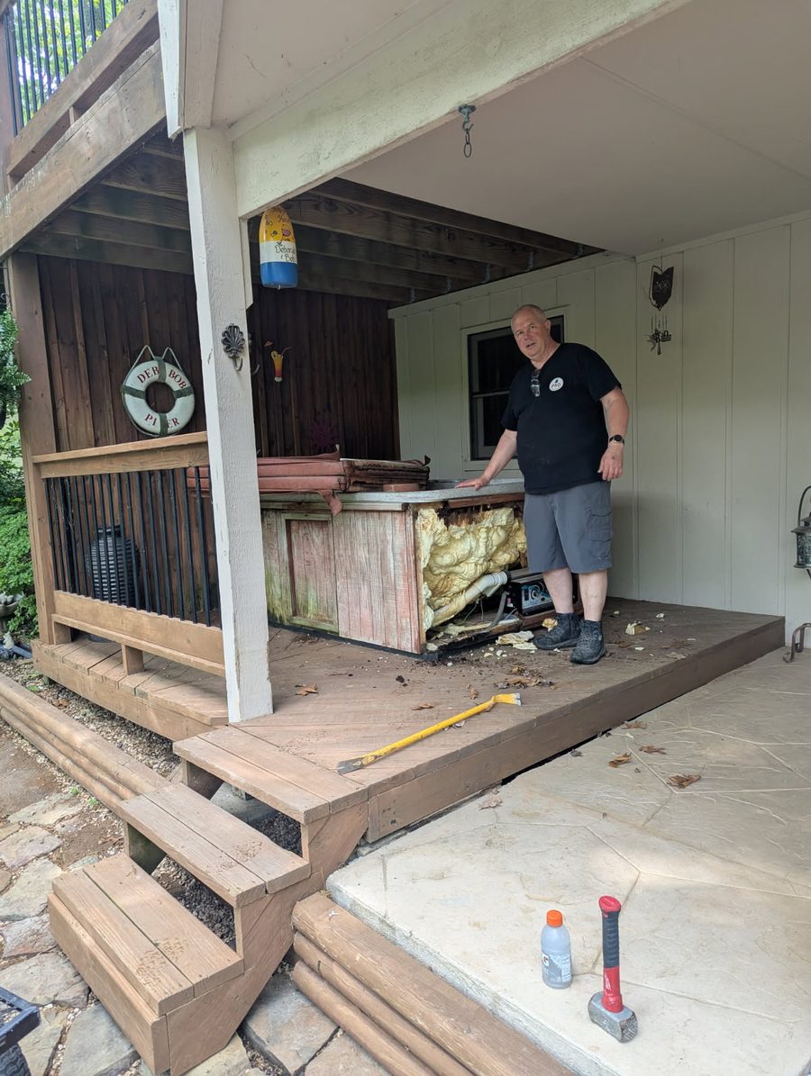 An old hot tub under a covered deck with its side panel pulled off, ready to be broken down and hauled away